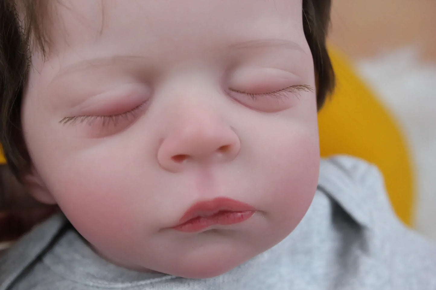 Lalka Reborn Lilli, realistyczne ciało z miękkiej tkaniny, ręcznie sadzone włosy i zamknięte oczy.