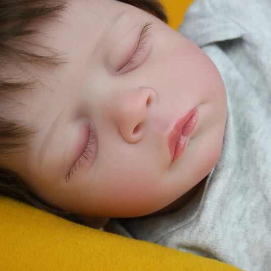 Lalka Reborn Lilli, realistyczne ciało z miękkiej tkaniny, ręcznie sadzone włosy i zamknięte oczy.